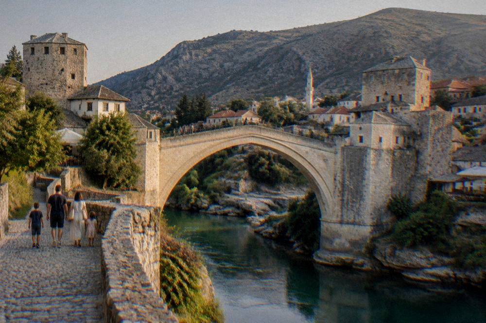 Family walking across a stone bridge in an old Balkan town in soft evening light