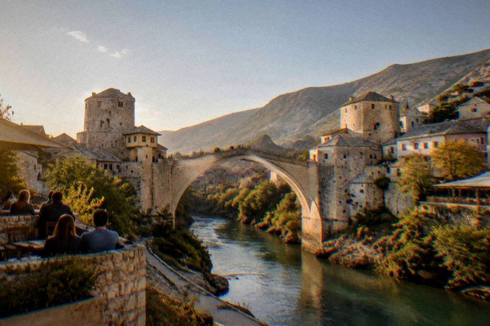 Crowds watching a diver leap from the Old Bridge into the Neretva on a sunny afternoon