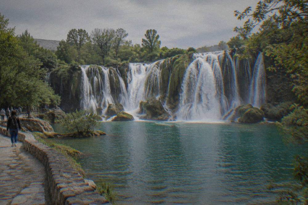 Wide waterfall curtain falling into a green pool at Kravica waterfall surrounded by trees