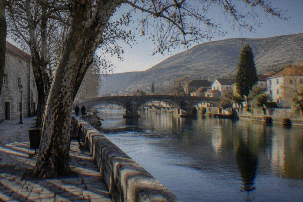 Stone buildings and plane trees along a small river in the old town of Trebinje