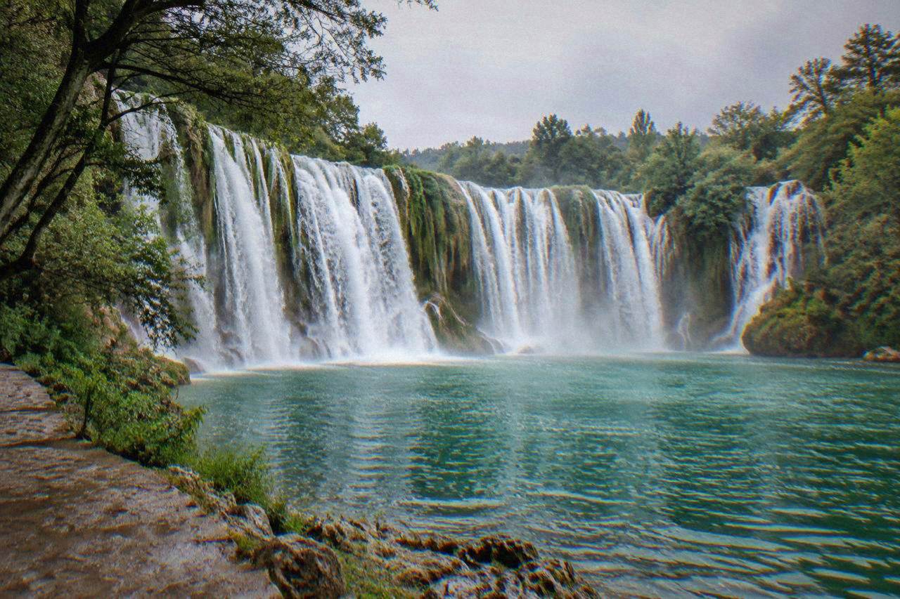 The wide travertine curtain of Kravica waterfall dropping into a green pool ringed by trees