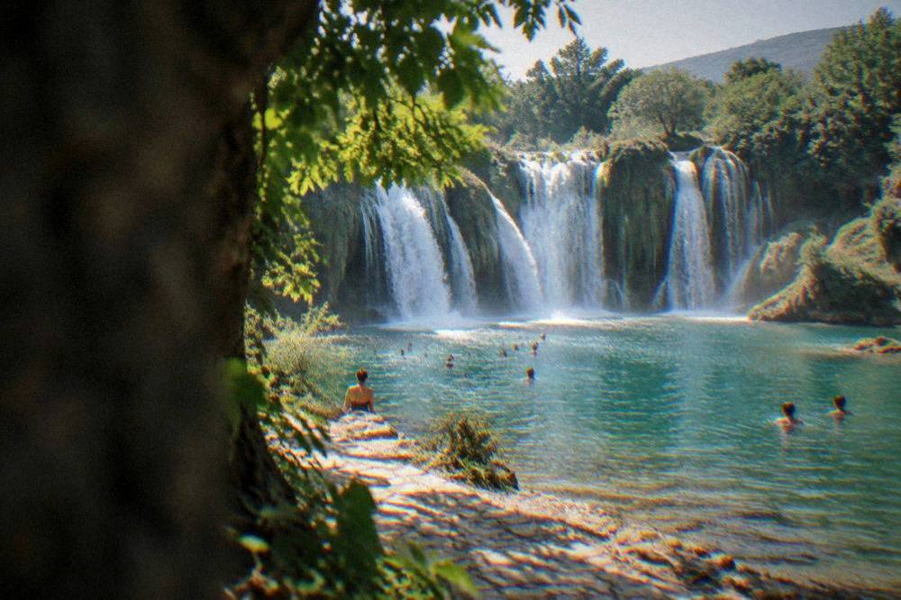 Swimmers in the pool beneath Kravica waterfall on a sunny afternoon