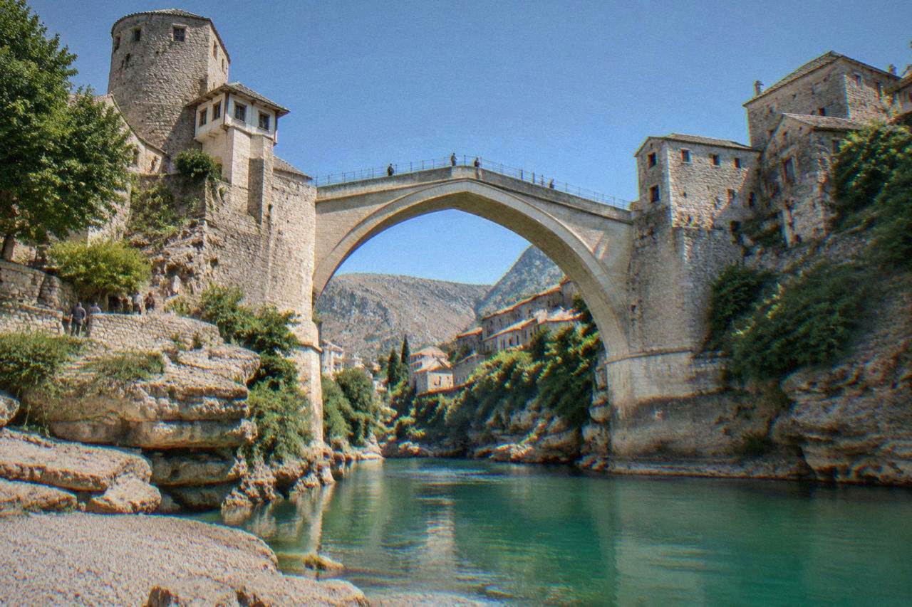The Old Bridge arching over the green Neretva river in Mostar at midday