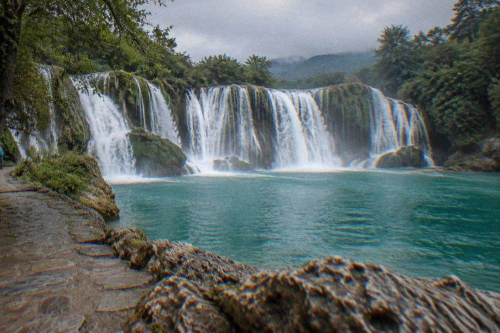Turquoise water cascading over the wide limestone ledge at Kravica waterfall