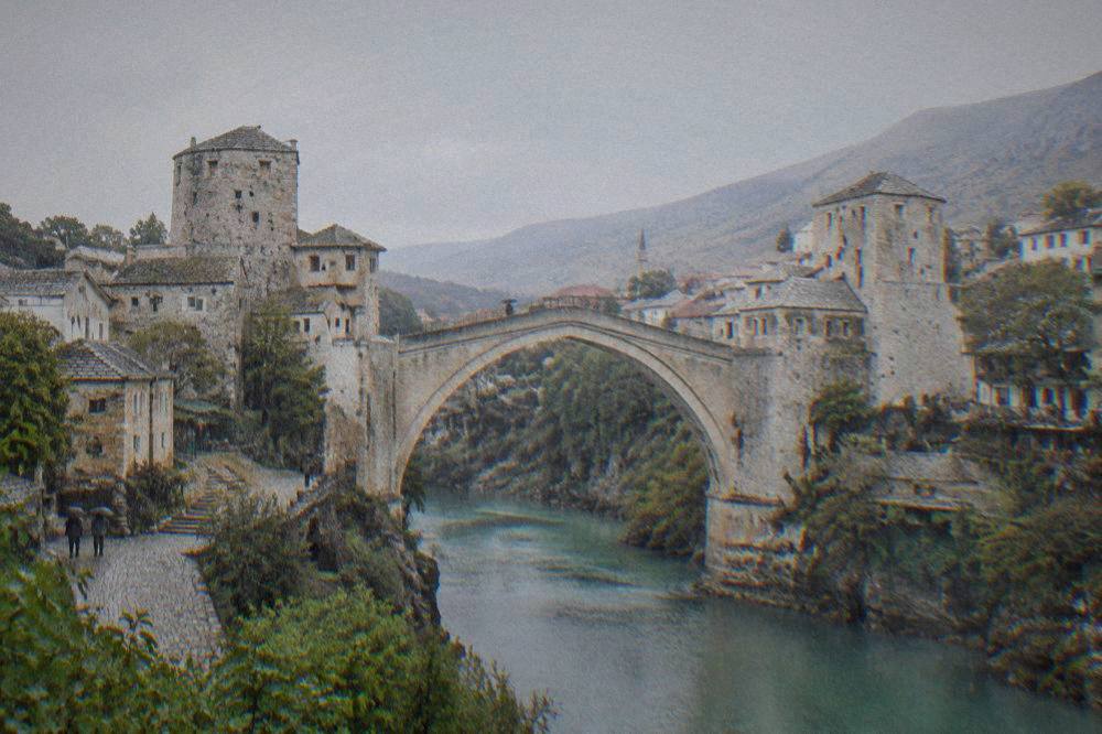 The wet stone arch of the Old Bridge in Mostar seen through falling rain