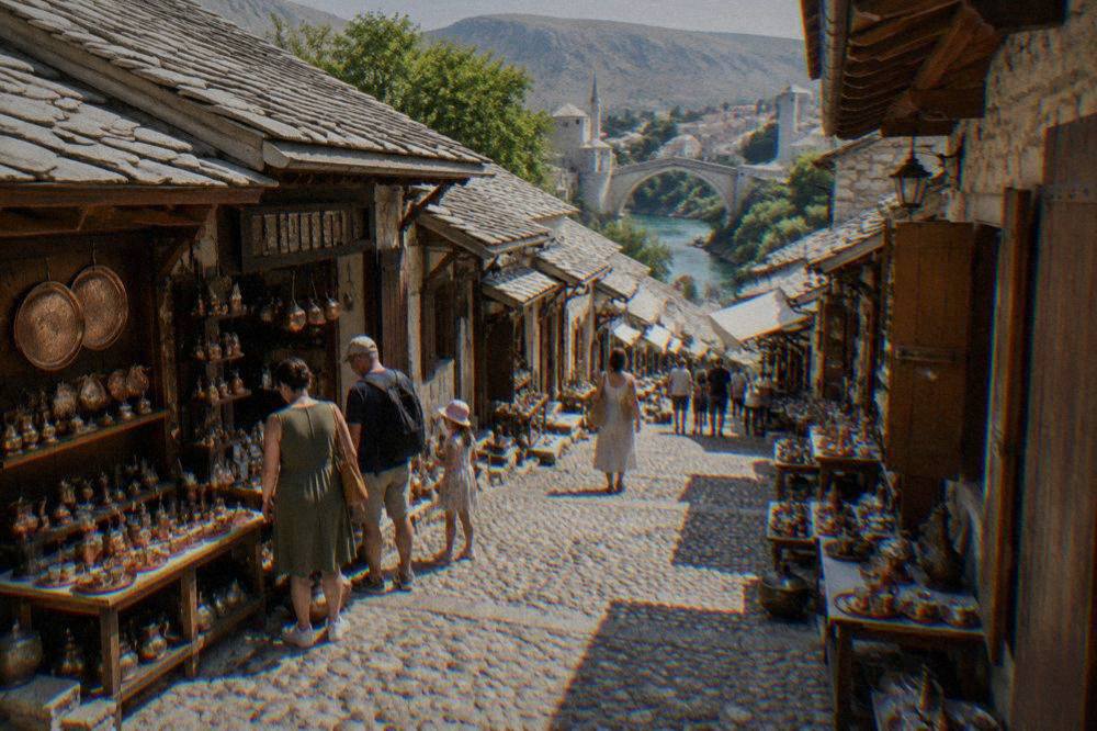 A narrow stone bazaar street with copper shops and families browsing