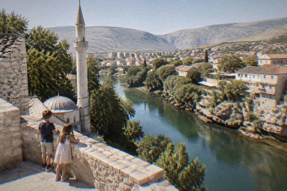 Children looking down at a river from a stone terrace beside a mosque minaret