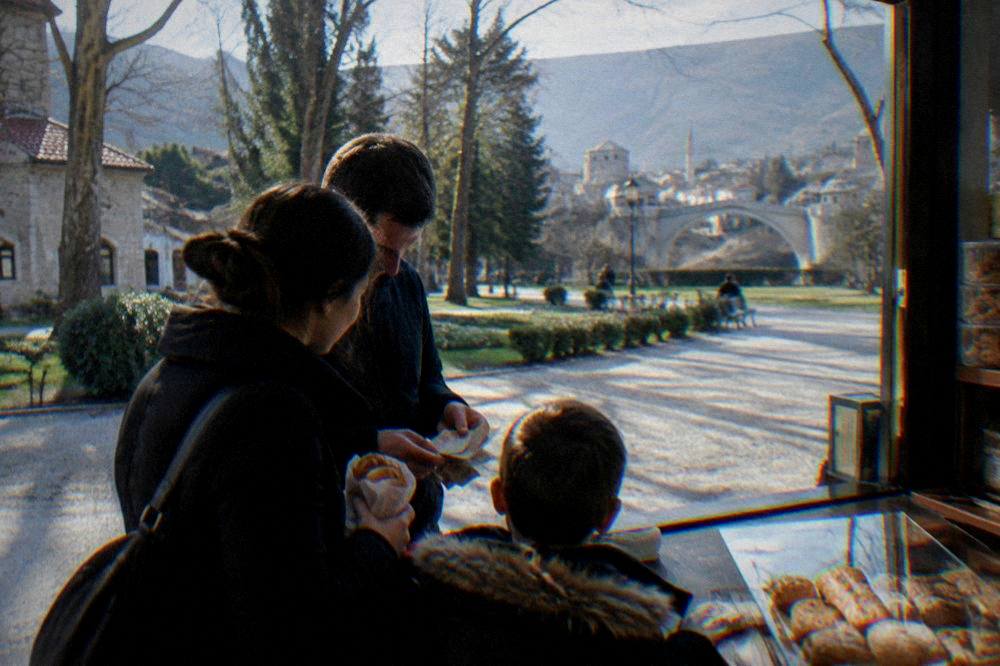 A family counting banknotes at a small shop counter with a pastry in hand