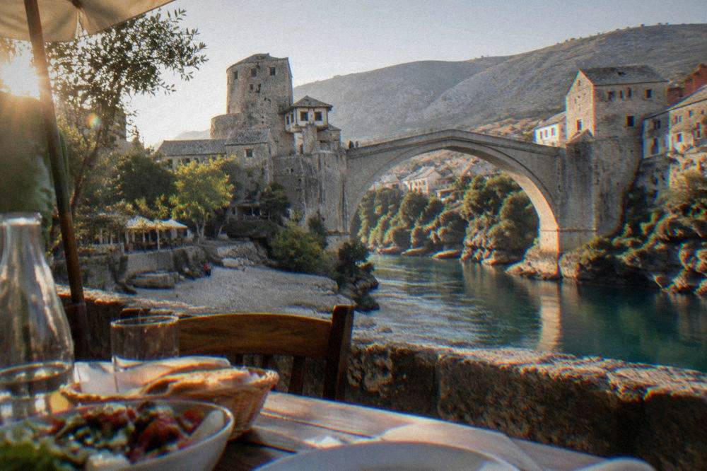 A riverside lunch table beside the Neretva with the stone bridge abutment behind