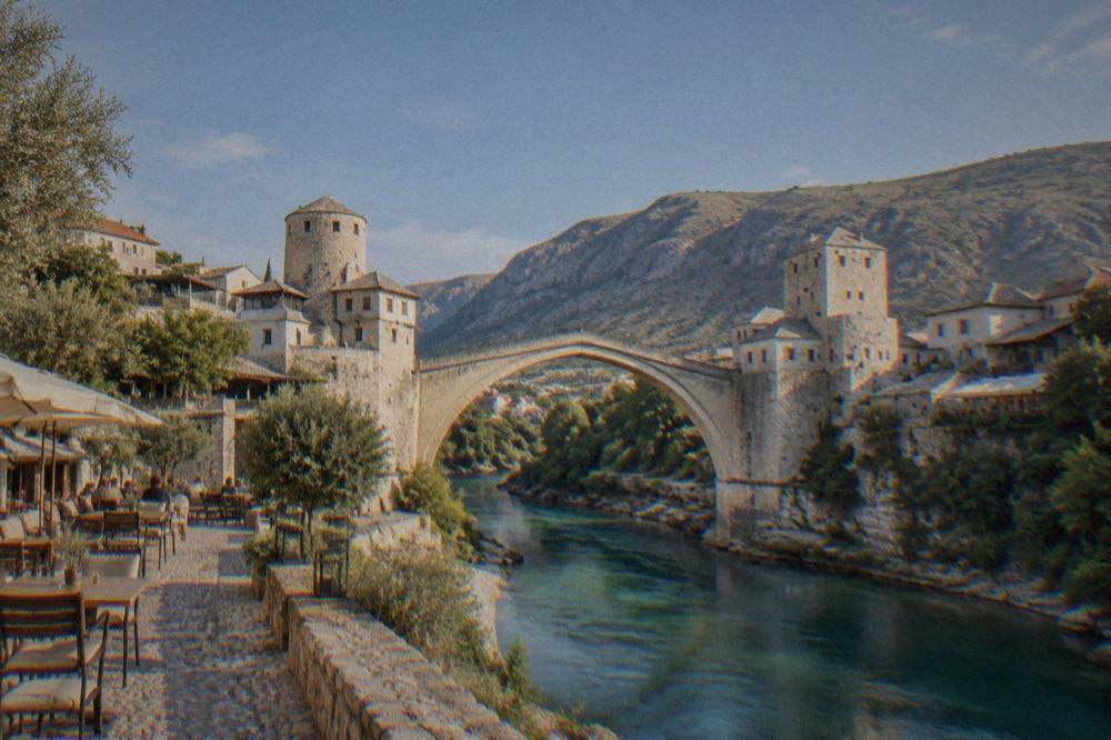 A stone lane on the south bank of the Neretva with cafe tables and olive sunlight