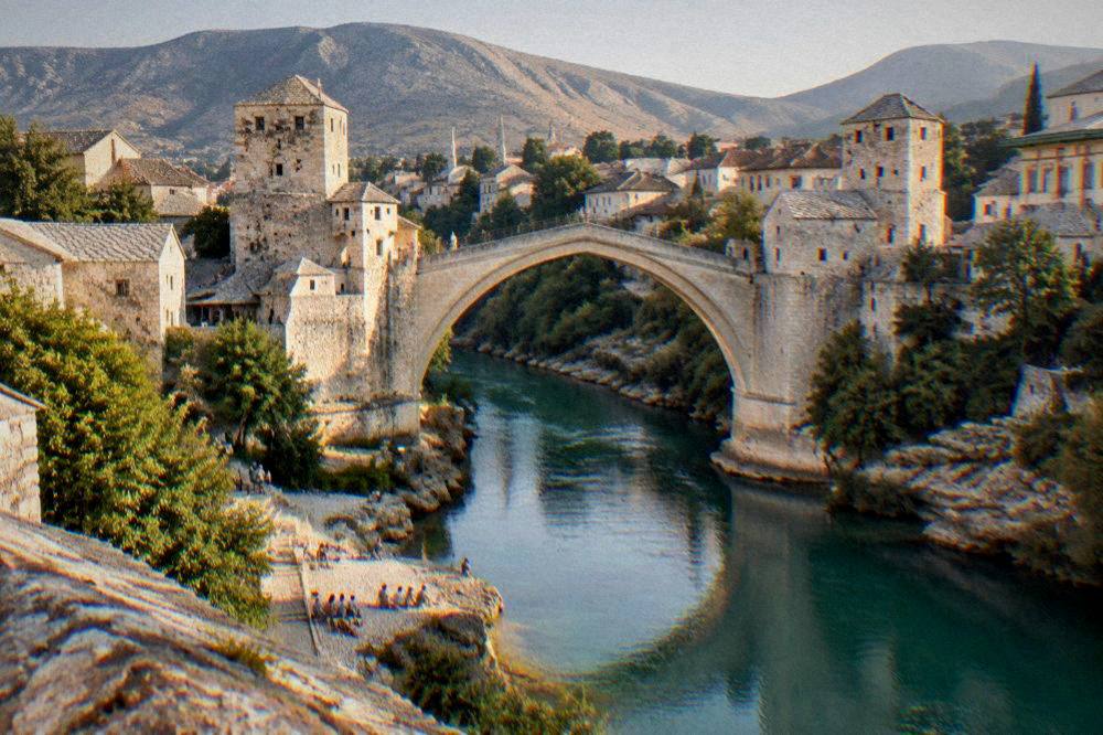 Warm evening light on the Old Bridge and the Neretva with people sitting on the riverbank