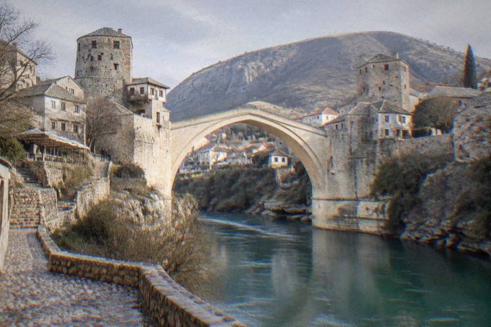 The stone arch of Stari Most seen from the river bank with cobbled streets above
