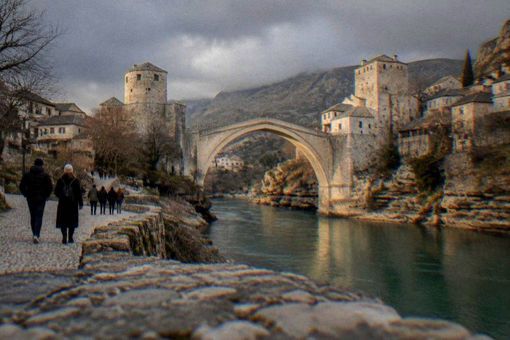 Visitors walking along the Neretva river bank toward the old bridge at dusk
