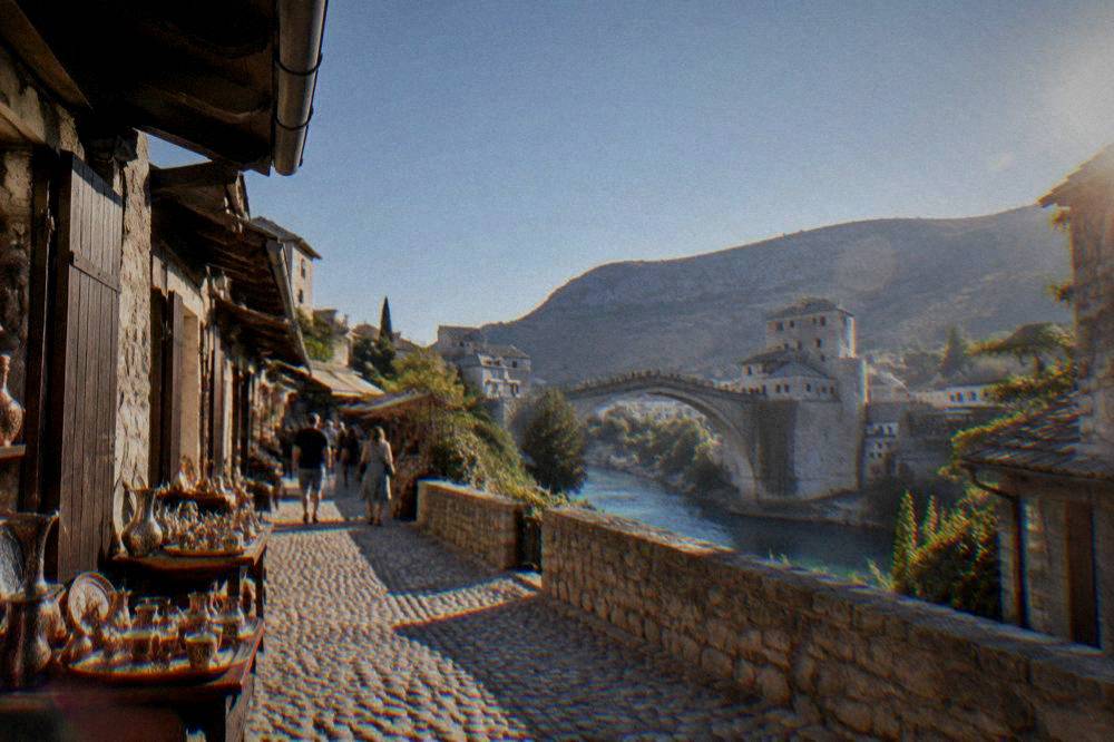 Tourists crossing a pale stone bridge under a clear blue morning sky
